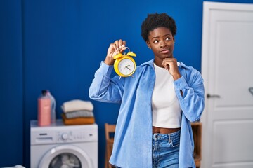 African american woman waiting for laundry serious face thinking about question with hand on chin, thoughtful about confusing idea