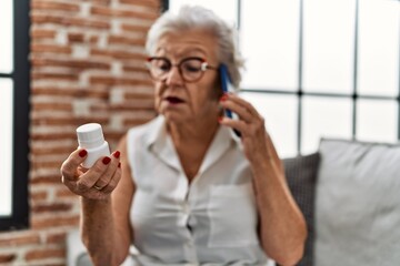 Senior grey-haired woman talking on the smartphone holding pills at home