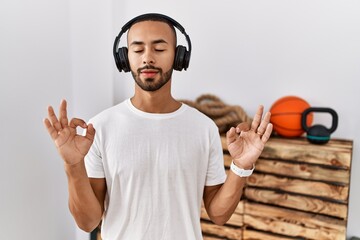 African american man listening to music using headphones at the gym relax and smiling with eyes closed doing meditation gesture with fingers. yoga concept.