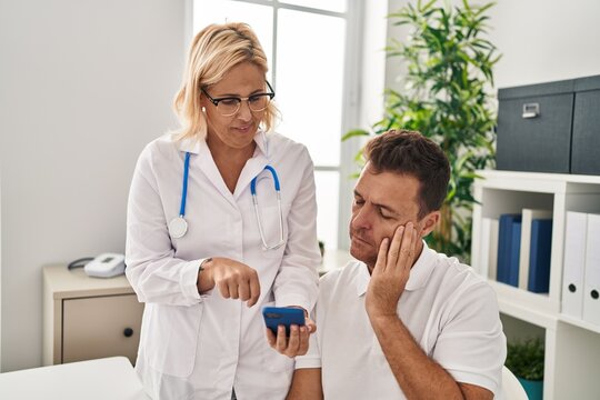 Middle Age Man And Woman Doctor And Patient Using Smartphone At Clinic