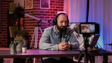Selective focus on male content creator streaming live internet vlog using digital video camera from home studio. Caucasian influencer recording podcast for social media channel using audio equipment.