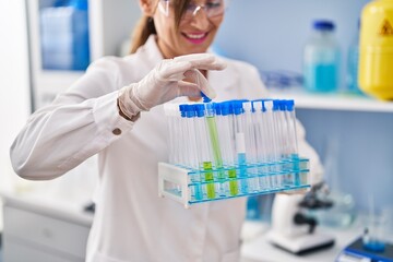 Middle age woman wearing scientist uniform holding test tubes at laboratory