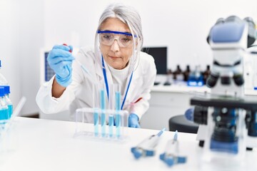 Middle age grey-haired woman wearing scientist uniform using pipette at laboratory