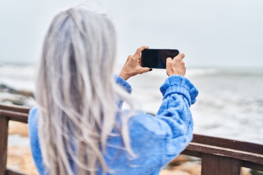 Middle age grey-haired woman make photo by smartphone at seaside