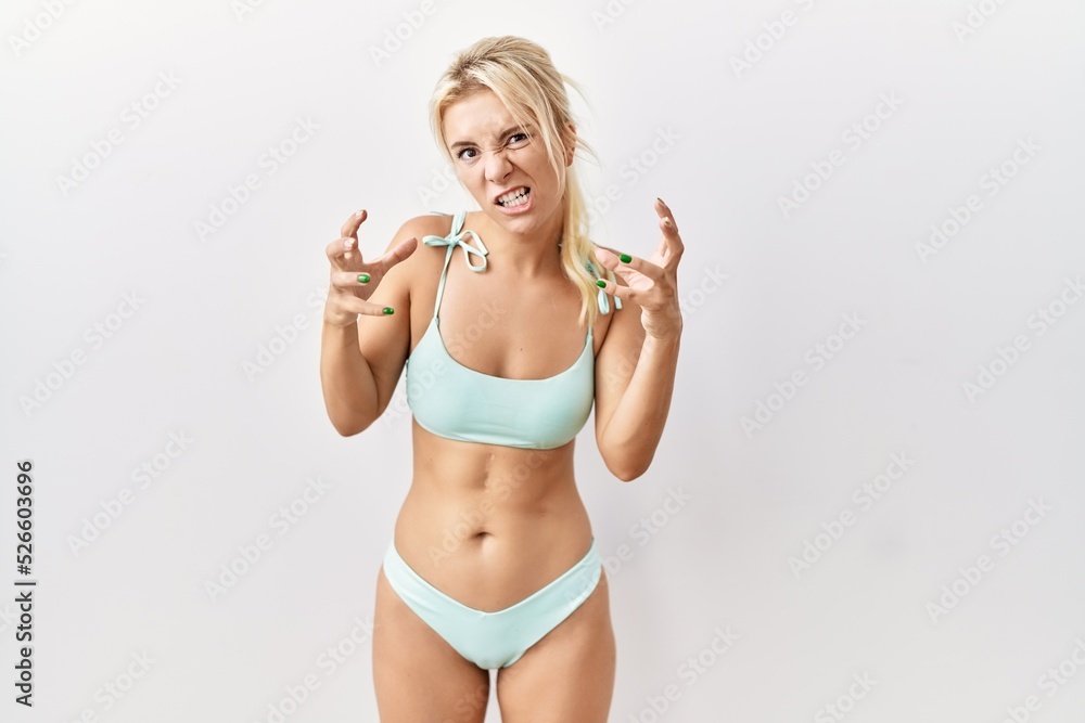 Wall mural young caucasian woman wearing bikini over isolated background shouting frustrated with rage, hands t