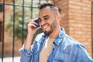 Young hispanic man smiling confident listening audio message by the smartphone at street
