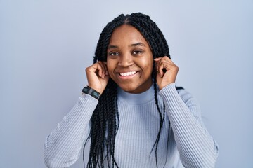 African american woman standing over blue background smiling pulling ears with fingers, funny...
