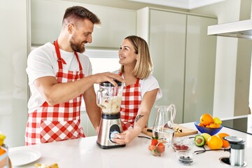 Young couple smiling confident making smoothie using blender at kitchen