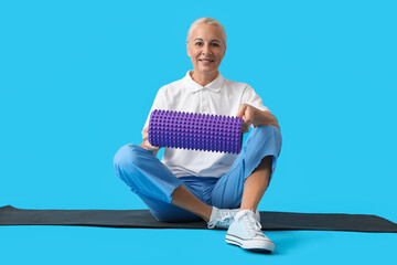 Mature physiotherapist with foam roller sitting on blue background