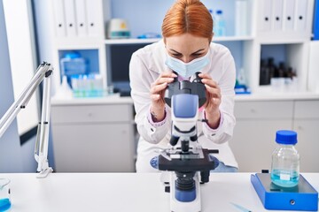 Young caucasian woman scientist wearing medical mask using microscope at laboratory