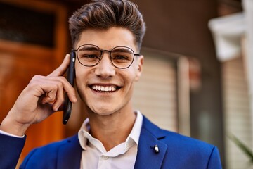 Young man talking on the smartphone wearing suit and glasses at street