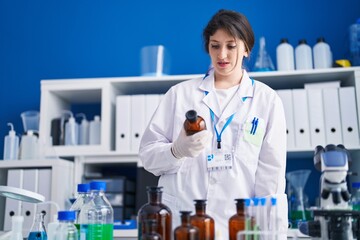 Young hispanic woman scientist holding bottle at laboratory