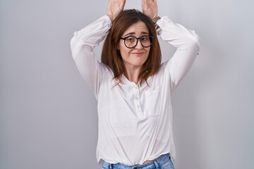 Brunette woman standing over white isolated background doing bunny ears gesture with hands palms looking cynical and skeptical. easter rabbit concept.