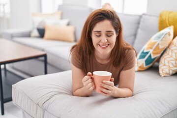 Young woman drinking coffee lying on sofa at home
