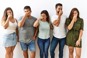 Group of young hispanic friends standing together over isolated background smelling something...