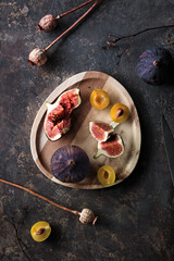 Autumn fruits, black fig and yellow plums on wooden tray. Flat lay, top view on dark textured background with dry poppy plants and hemp cord. Fruits in Fall season.