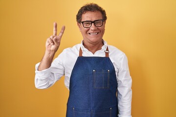 Middle age hispanic man wearing professional cook apron showing and pointing up with fingers number...