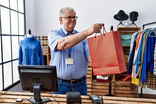 Middle age grey-haired man holding shopping bag working at clothing store