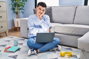 Non binary person studying using computer laptop sitting on the floor thinking looking tired and bored with depression problems with crossed arms.