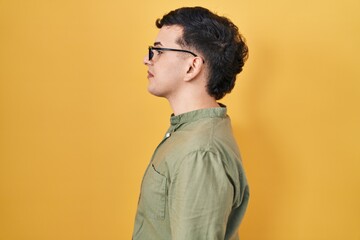 Non binary person standing over yellow background looking to side, relax profile pose with natural...