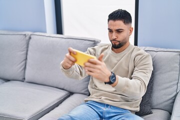 Young arab man playing video game sitting on sofa at home