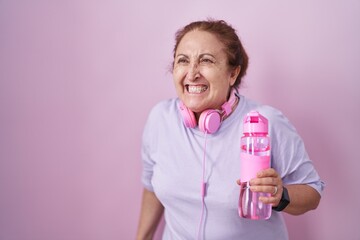 Senior woman wearing sportswear and headphones angry and mad screaming frustrated and furious,...