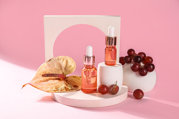 Composition with bottles of essential oil, grapes and plaster decor on pink background