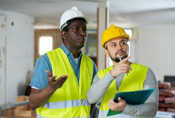 Portrait of man builder and foreman discussing working process at indoor construction site