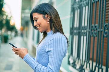 Young hispanic woman using smartphone at the town