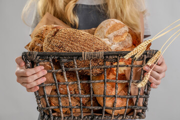 Young woman holding basket with fresh bread on grey background, closeup
