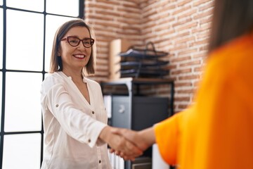 Two women business workers smiling confident shake hands at office