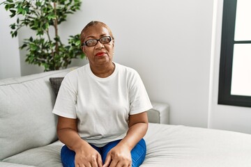 Mature hispanic woman sitting on the sofa at home relaxed with serious expression on face. simple...