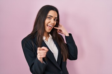 Fototapeta na wymiar Young brunette woman wearing business style over pink background smiling doing talking on the telephone gesture and pointing to you. call me.