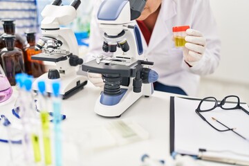 Middle age hispanic woman wearing scientist uniform analysing urine test using microscope at laboratory