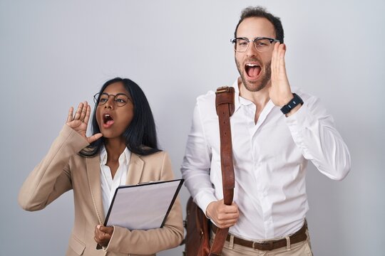 Interracial business couple wearing glasses shouting and screaming loud to side with hand on mouth. communication concept.