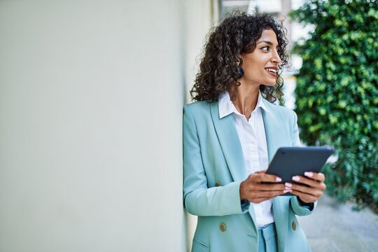 Young hispanic business woman wearing professional look smiling confident at the city using touchpad device