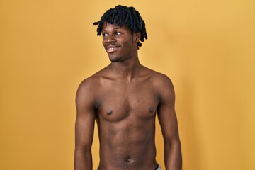 Fototapeta premium Young african man with dreadlocks standing shirtless looking away to side with smile on face, natural expression. laughing confident.