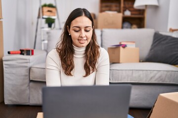 Young beautiful hispanic woman smiling confident using laptop at new home