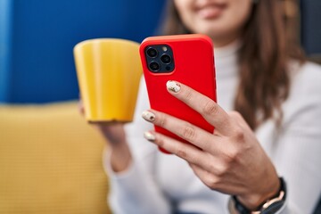 Young beautiful hispanic woman using smartphone drinking coffee at home