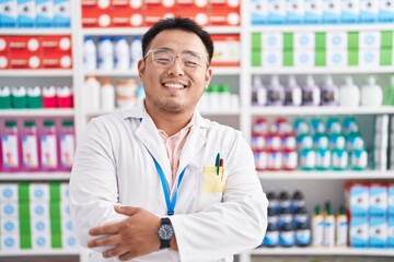 Chinese young man working at pharmacy drugstore happy face smiling with crossed arms looking at the camera. positive person.