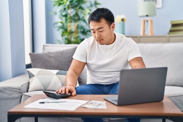 Young chinese man accounting economy using laptop and calculator at home