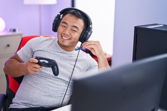 Young chinese man streamer playing video game using joystick at gaming room