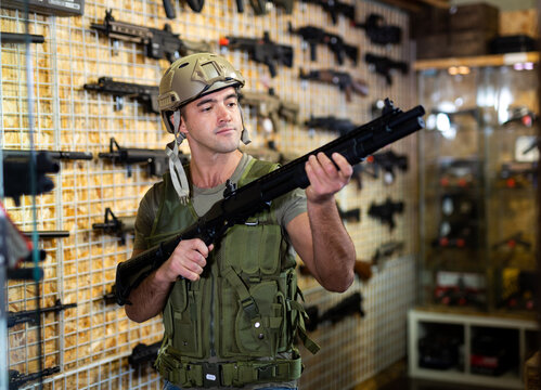 European man in armor vest standing in salesroom of gun shop and selecting machine gun.
