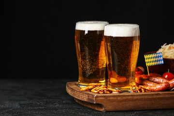 Board with glasses of beer, food and flags on table against dark background. Oktoberfest celebration