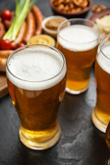 Mugs of fresh beer and traditional food on dark background, closeup. Oktoberfest celebration
