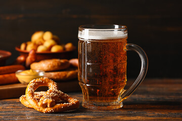 Mug of fresh beer with pretzel on table against dark background, closeup. Oktoberfest celebration