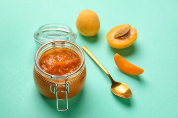 Glass jar of tasty apricot jam on color background