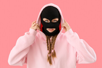 Young woman in balaclava adjusting hood on pink background