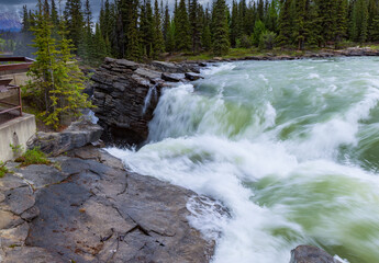 Top of green mountain waterfall with forest background and part of viewing area