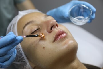 Cosmetologist applying cosmetic product for chemical peeling on client's face in salon